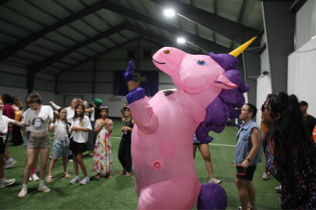 People dancing around a pink unicorn at a camp dance